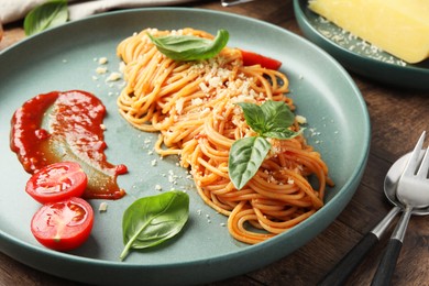 Delicious pasta with tomato sauce, basil and cheese served on wooden table, closeup