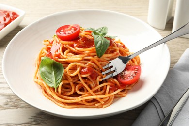 Photo of Taking delicious pasta with tomato sauce and basil at wooden table, closeup