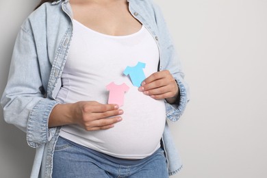 Photo of Pregnant woman with paper T-shirts on light gray background, closeup and space for text. Expecting twins