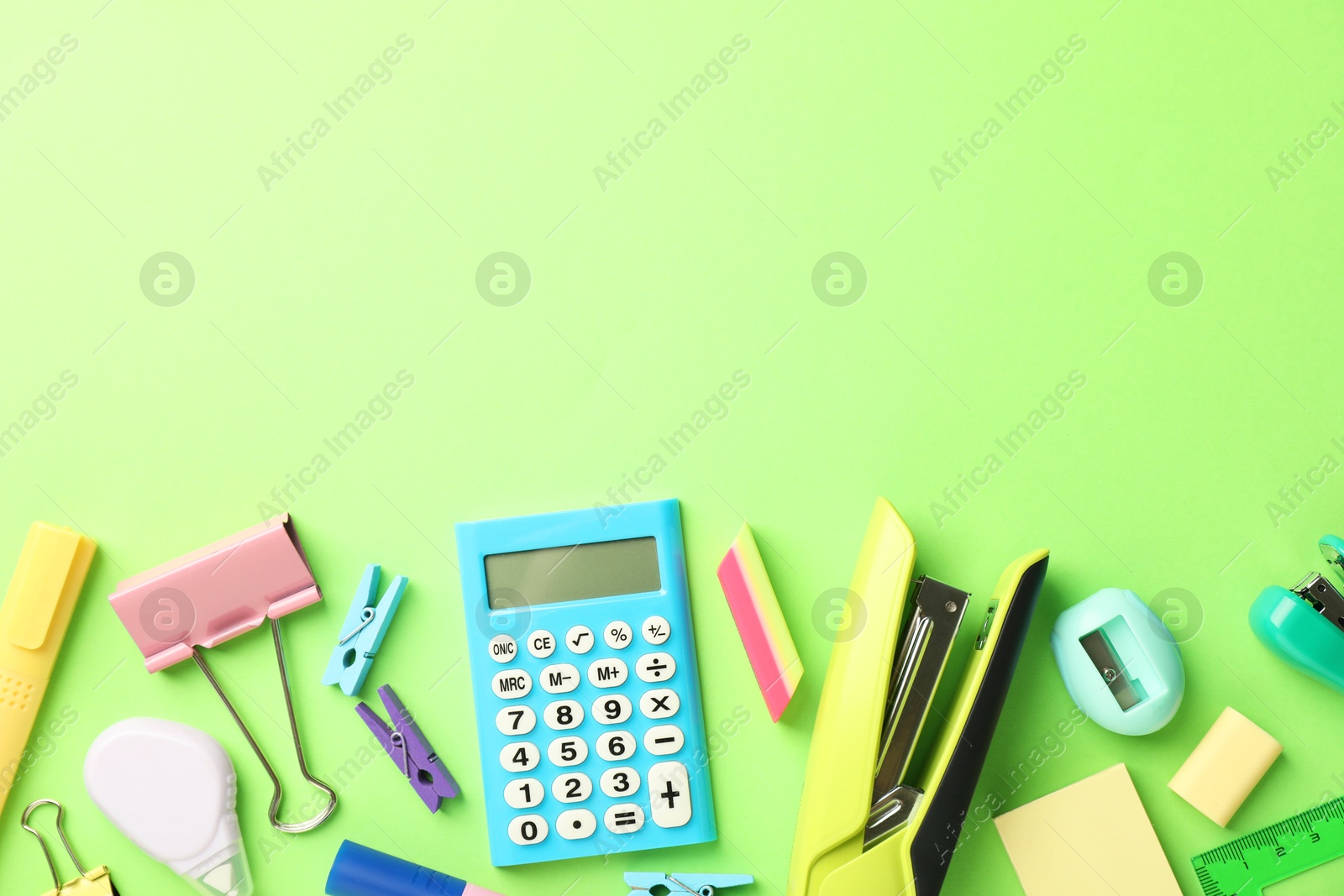 Photo of Bright staplers and other stationery on green background, flat lay. Space for text