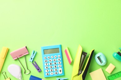 Bright staplers and other stationery on green background, flat lay. Space for text