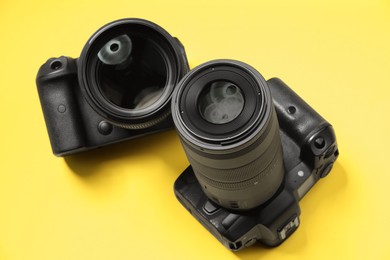 Photo of Two modern photo cameras on yellow background, above view