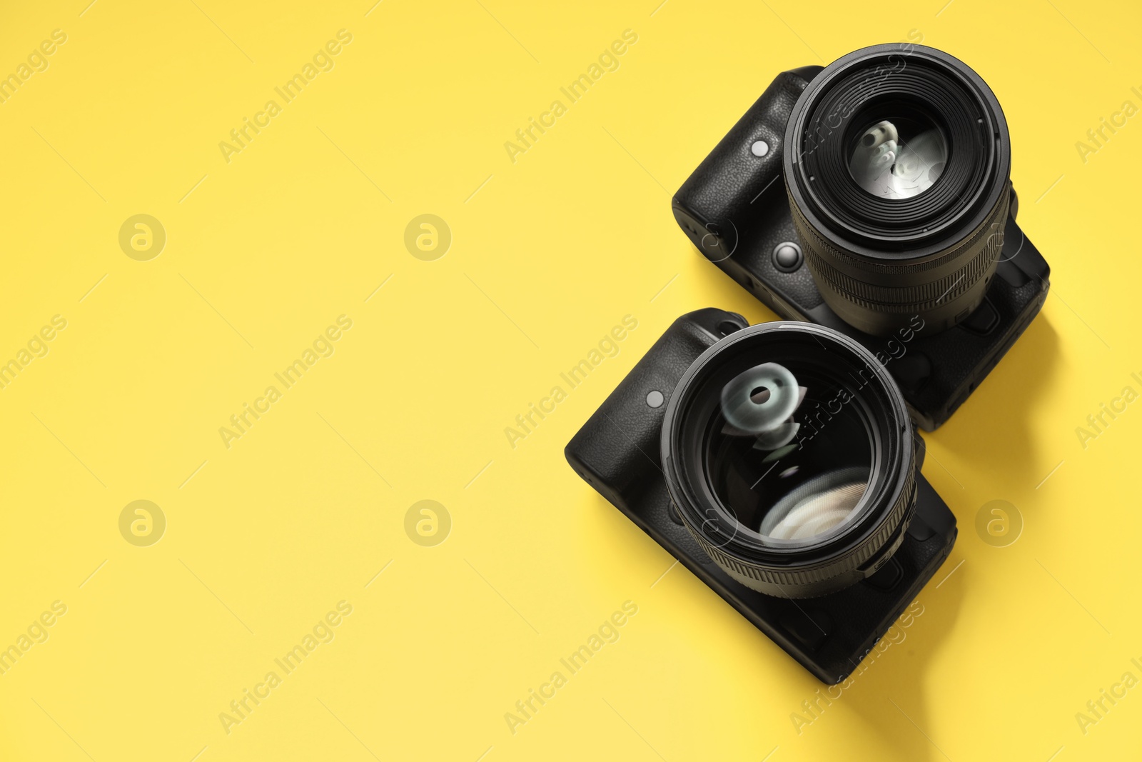 Photo of Two modern photo cameras on yellow background, above view. Space for text