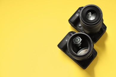 Two modern photo cameras on yellow background, above view. Space for text