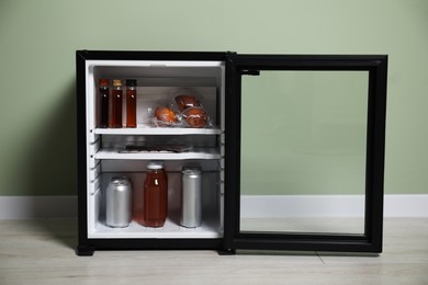 Photo of Mini refrigerator with different drinks and snacks near olive wall