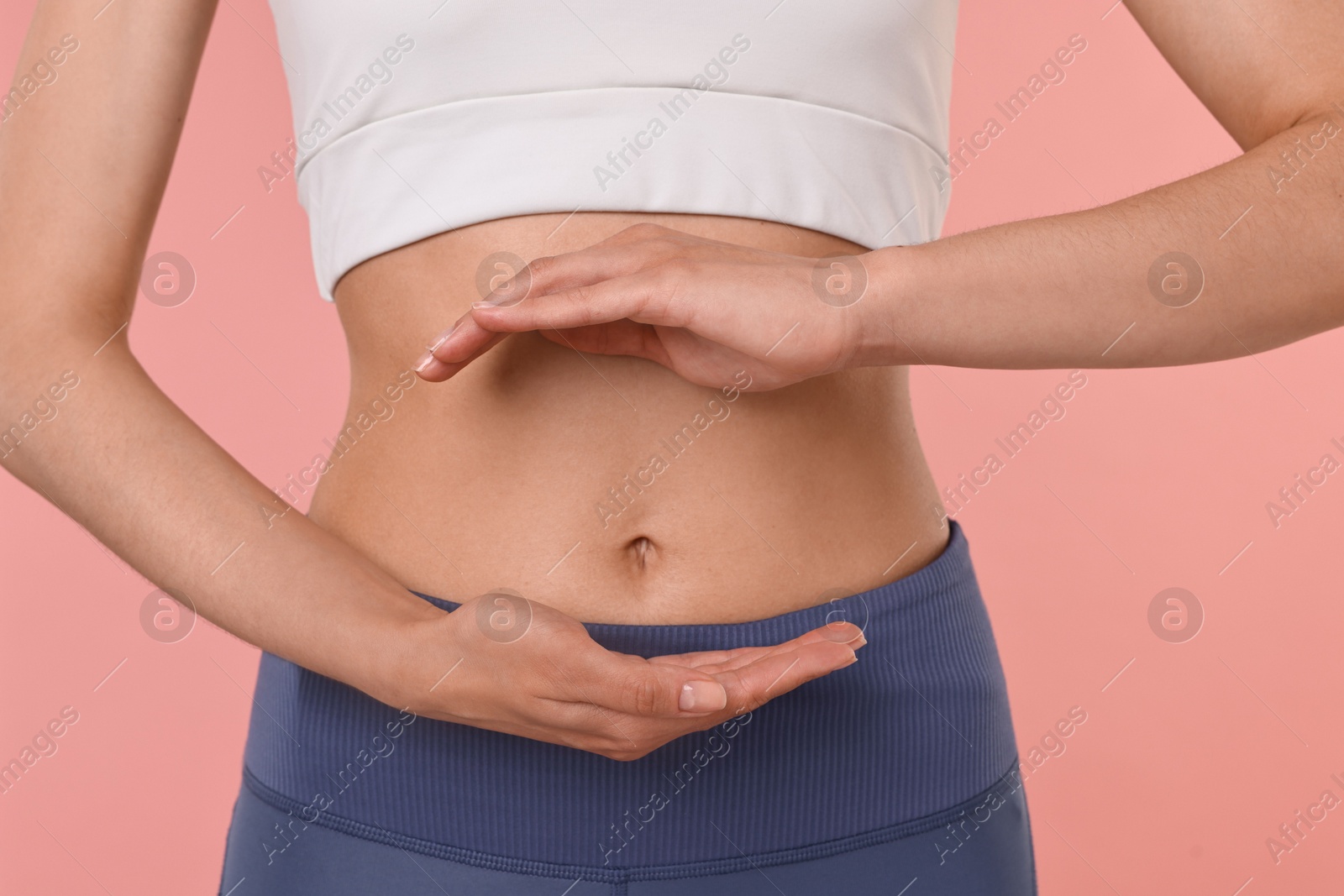 Photo of Healthy digestion. Woman holding something near her belly on pink background, closeup