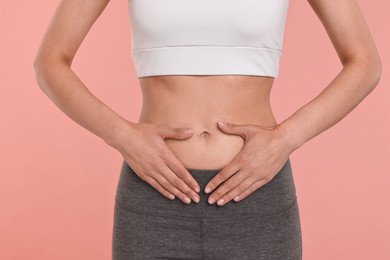 Healthy digestion. Woman making heart shape with hands near her belly on pink background, closeup