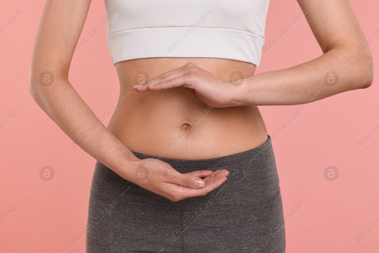 Photo of Healthy digestion. Woman holding something near her belly on pink background, closeup