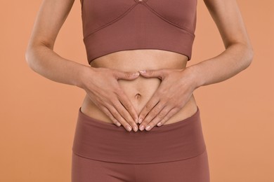 Photo of Healthy digestion. Woman making heart shape with hands near her belly on beige background, closeup