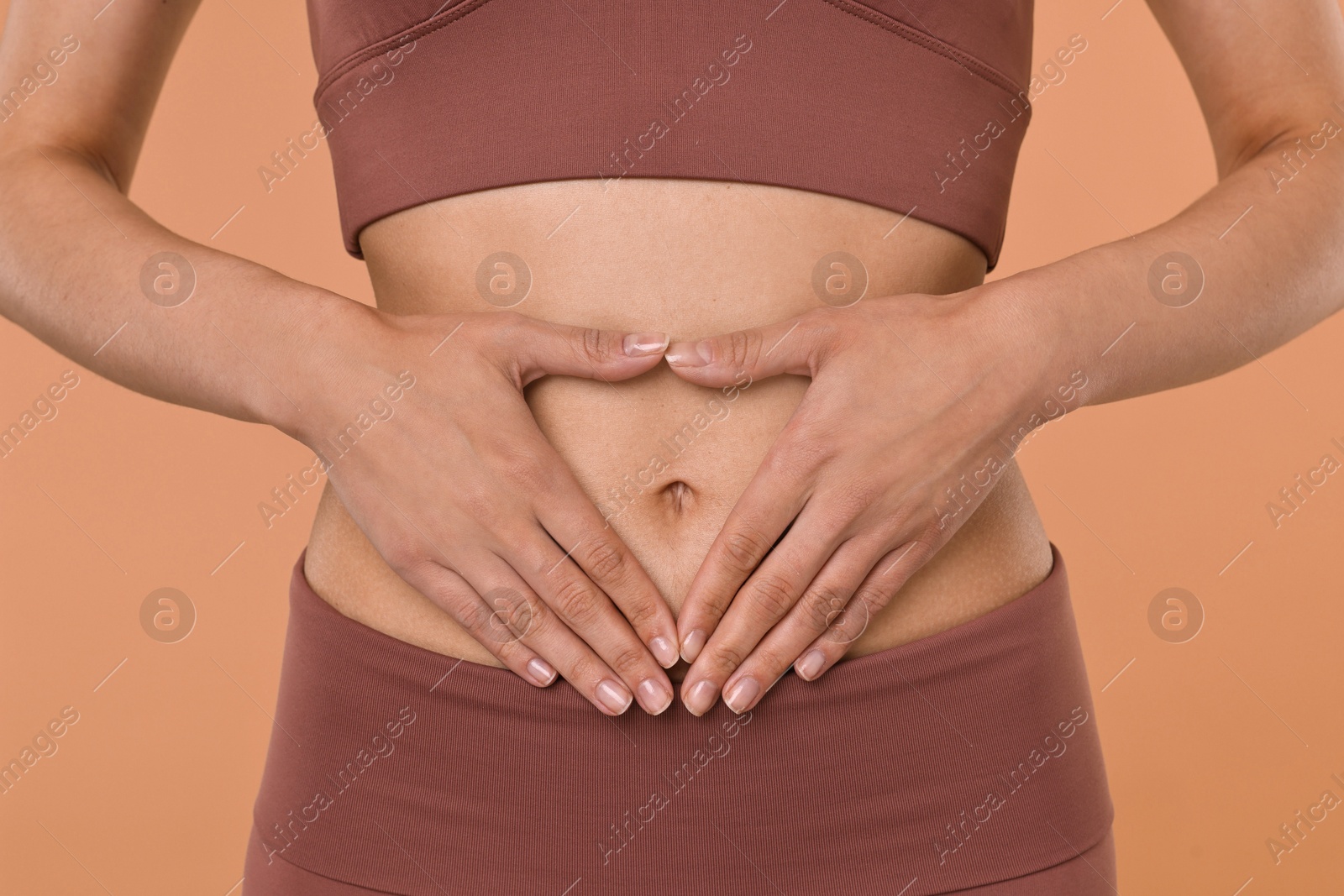 Photo of Healthy digestion. Woman making heart shape with hands near her belly on beige background, closeup