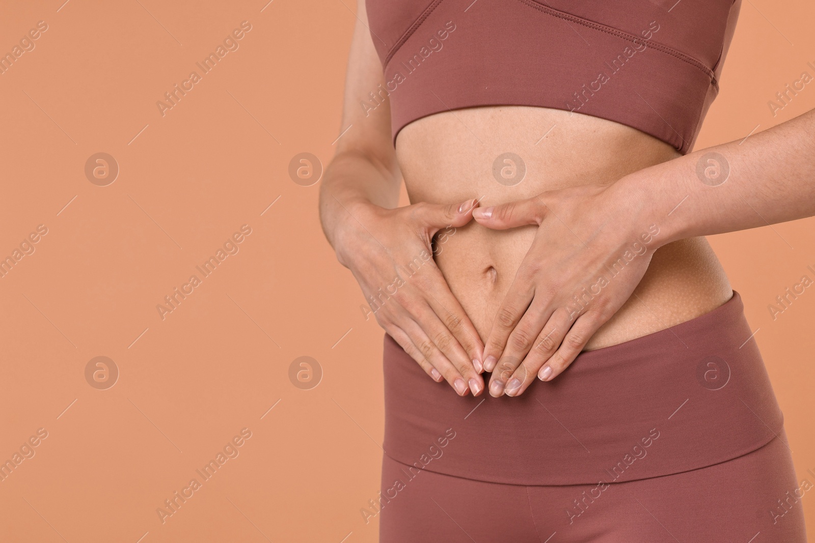 Photo of Healthy digestion. Woman making heart shape with hands near her belly on beige background, closeup. Space for text