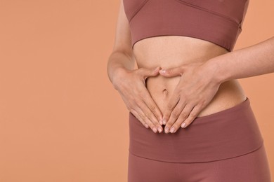 Photo of Healthy digestion. Woman making heart shape with hands near her belly on beige background, closeup. Space for text