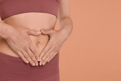 Photo of Healthy digestion. Woman making heart shape with hands near her belly on beige background, closeup. Space for text