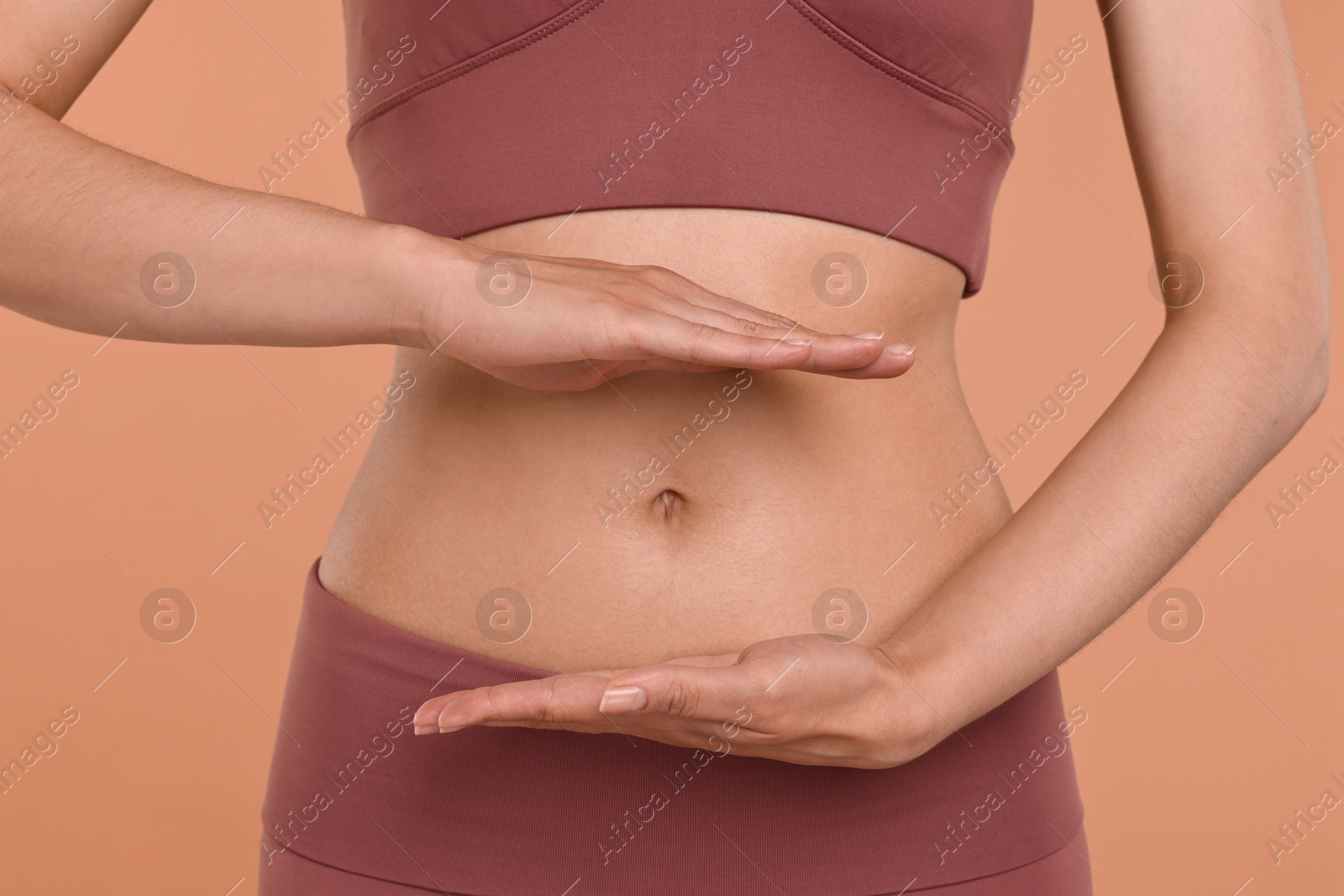 Photo of Healthy digestion. Woman holding something near her belly on beige background, closeup