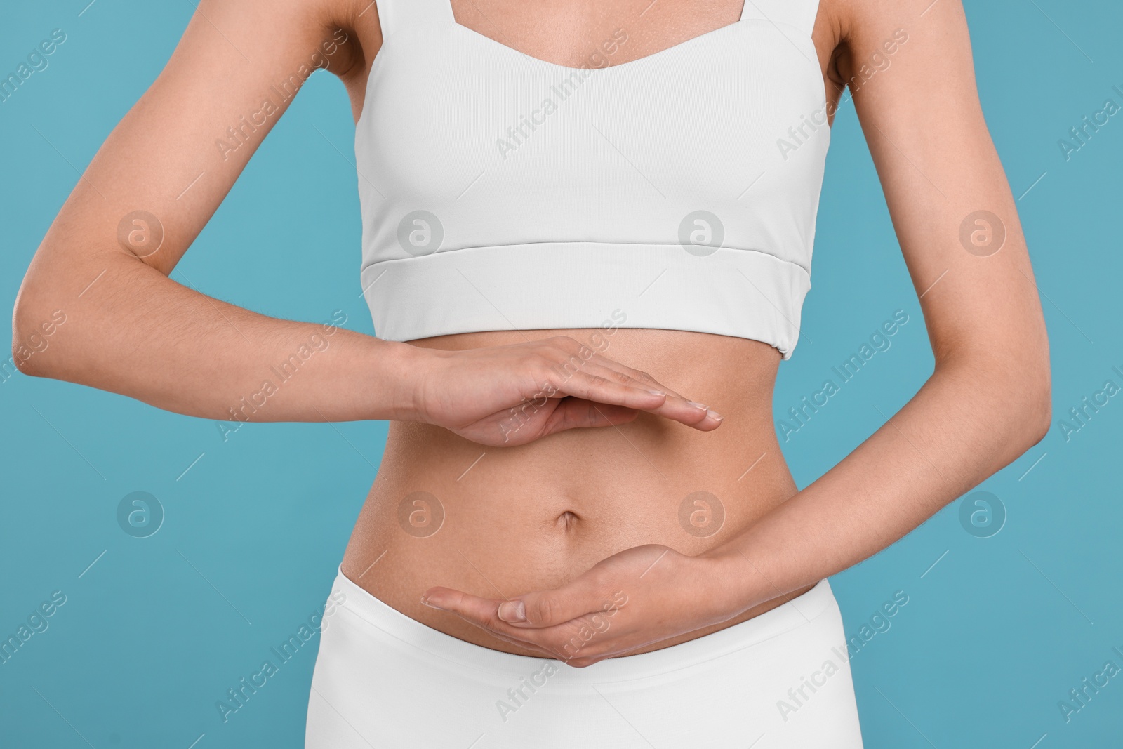 Photo of Healthy digestion. Woman holding something near her belly on light blue background, closeup