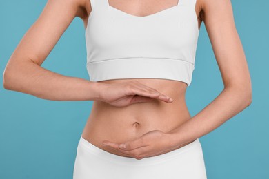 Healthy digestion. Woman holding something near her belly on light blue background, closeup