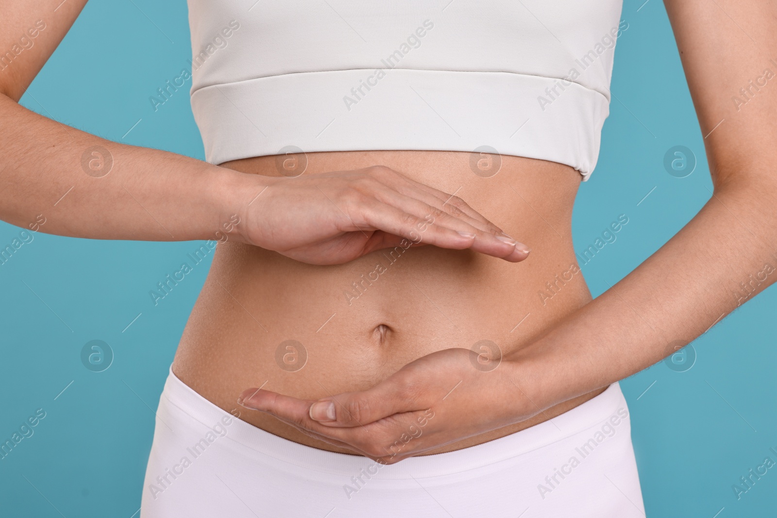 Photo of Healthy digestion. Woman holding something near her belly on light blue background, closeup