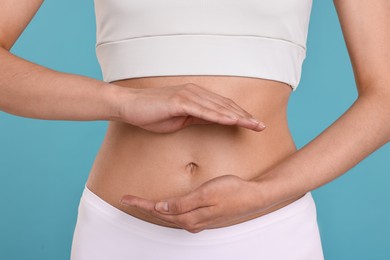 Photo of Healthy digestion. Woman holding something near her belly on light blue background, closeup