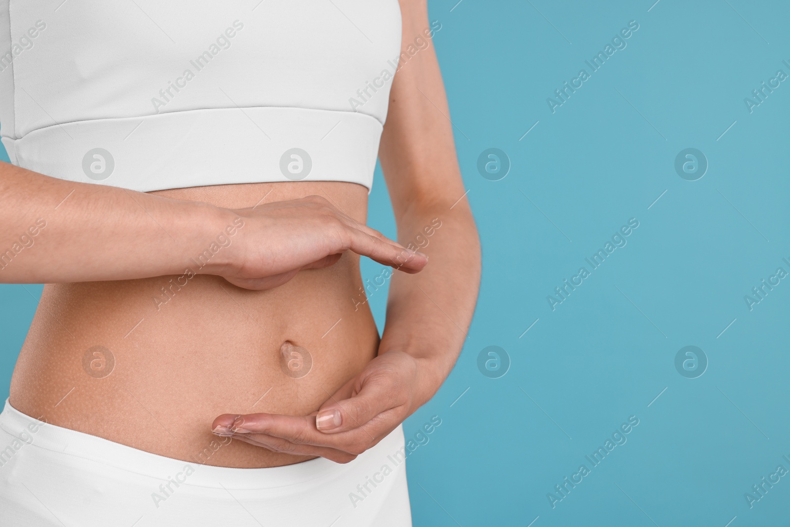 Photo of Healthy digestion. Woman holding something near her belly on light blue background, closeup. Space for text