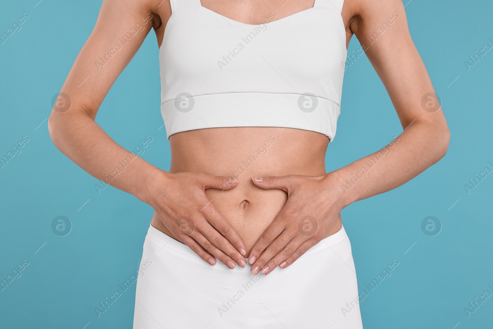 Photo of Healthy digestion. Woman making heart shape with hands near her belly on light blue background, closeup