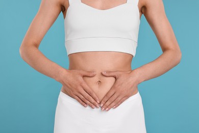 Healthy digestion. Woman making heart shape with hands near her belly on light blue background, closeup