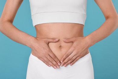 Photo of Healthy digestion. Woman making heart shape with hands near her belly on light blue background, closeup