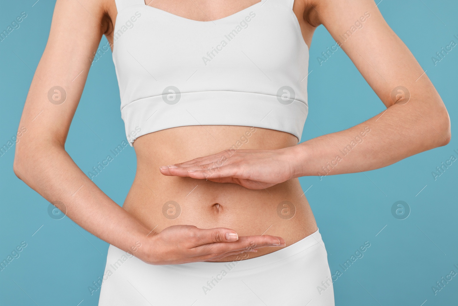 Photo of Healthy digestion. Woman holding something near her belly on light blue background, closeup