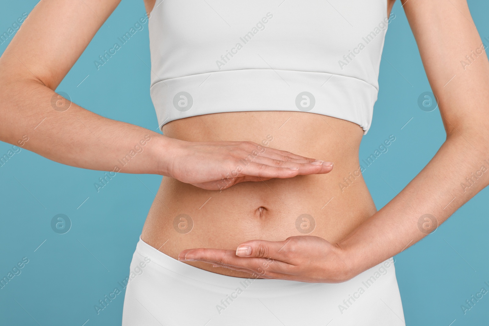 Photo of Healthy digestion. Woman holding something near her belly on light blue background, closeup