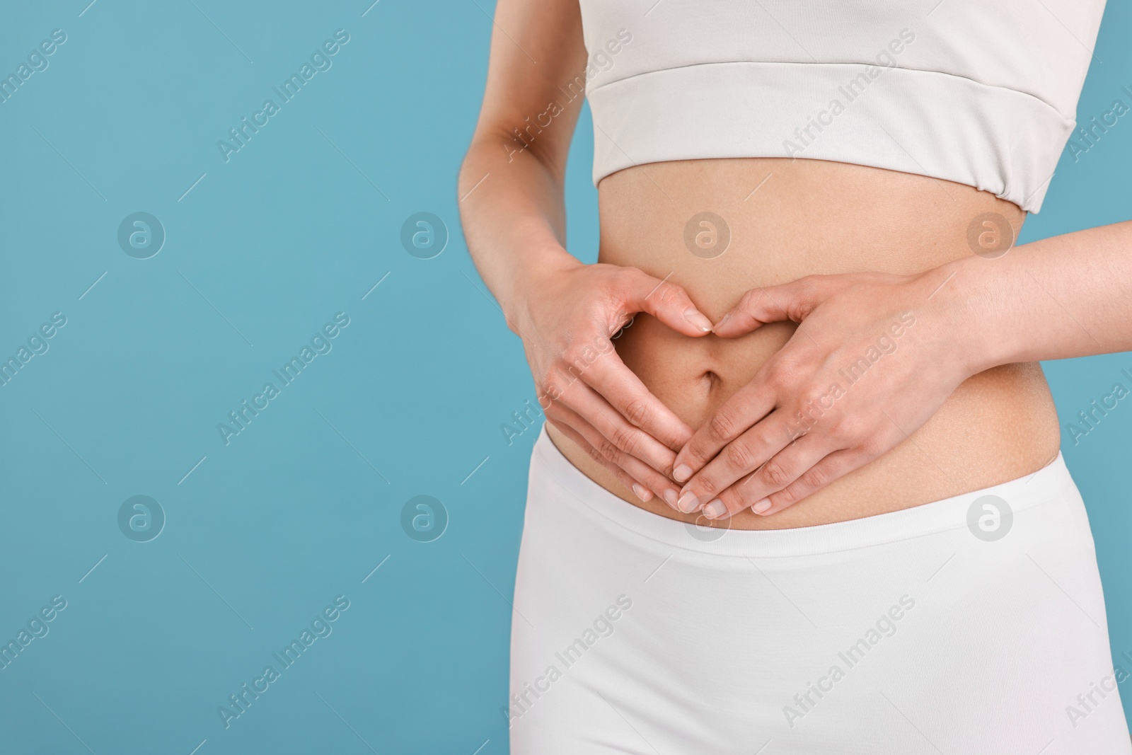 Photo of Healthy digestion. Woman making heart shape with hands near her belly on light blue background, closeup. Space for text