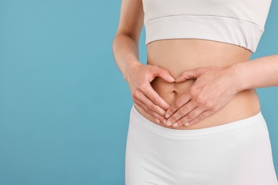 Photo of Healthy digestion. Woman making heart shape with hands near her belly on light blue background, closeup. Space for text