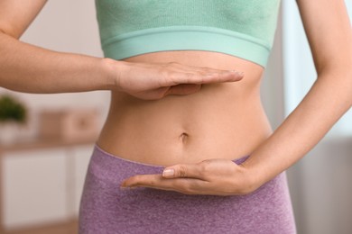 Healthy digestion. Woman holding something near her belly indoors, closeup