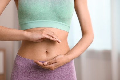 Photo of Healthy digestion. Woman holding something near her belly indoors, closeup