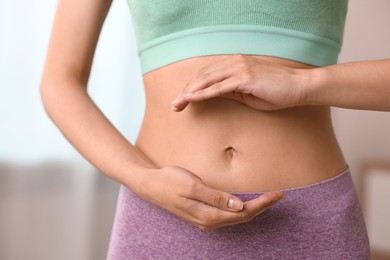 Healthy digestion. Woman holding something near her belly indoors, closeup