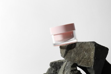 Face cream in jar on stones against light background, space for text