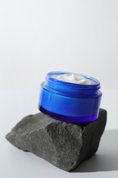 Face cream in jar on stone against light background