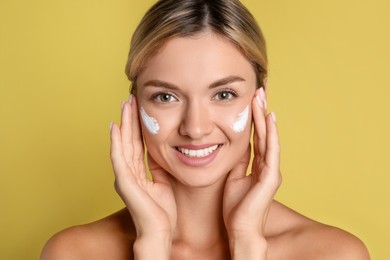 Beautiful woman with cream on her face against olive background