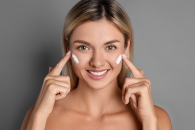 Photo of Beautiful woman applying face cream on grey background