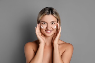 Beautiful woman with cream on her face against grey background