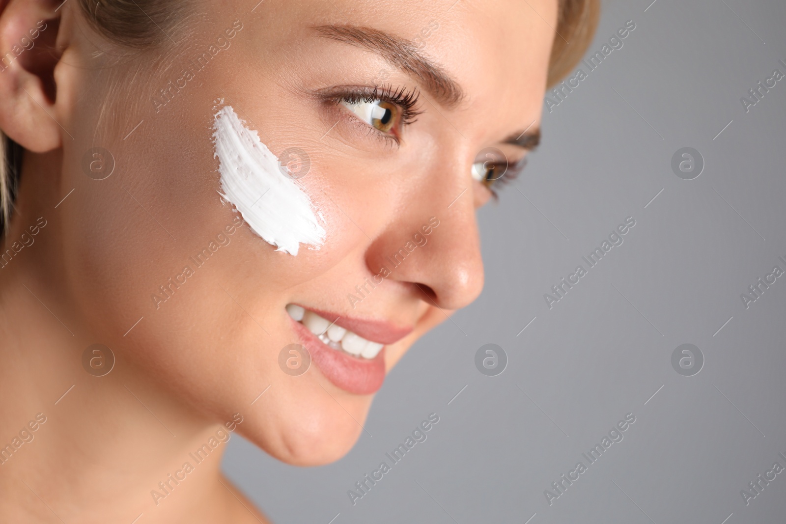 Photo of Beautiful woman with cream on her face against grey background, closeup. Space for text