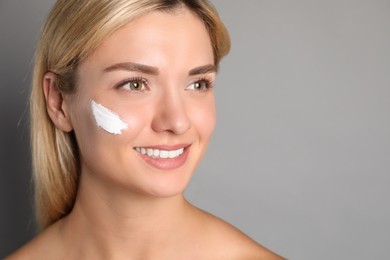 Photo of Beautiful woman with cream on her face against grey background, closeup. Space for text