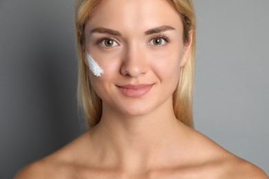 Beautiful woman with cream on her face against grey background, closeup