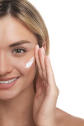 Beautiful woman with cream on her face against white background, closeup