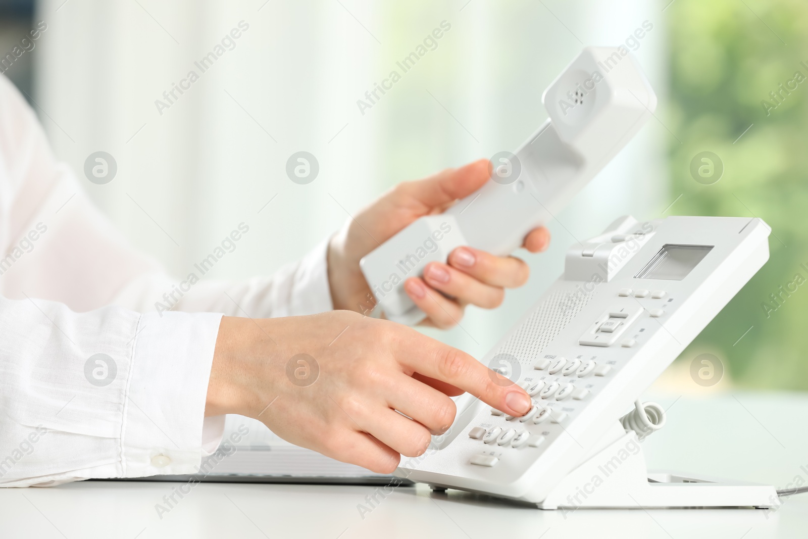 Photo of Assistant dialing number on telephone against blurred background, closeup