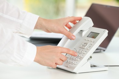 Assistant dialing number on telephone at white table, closeup