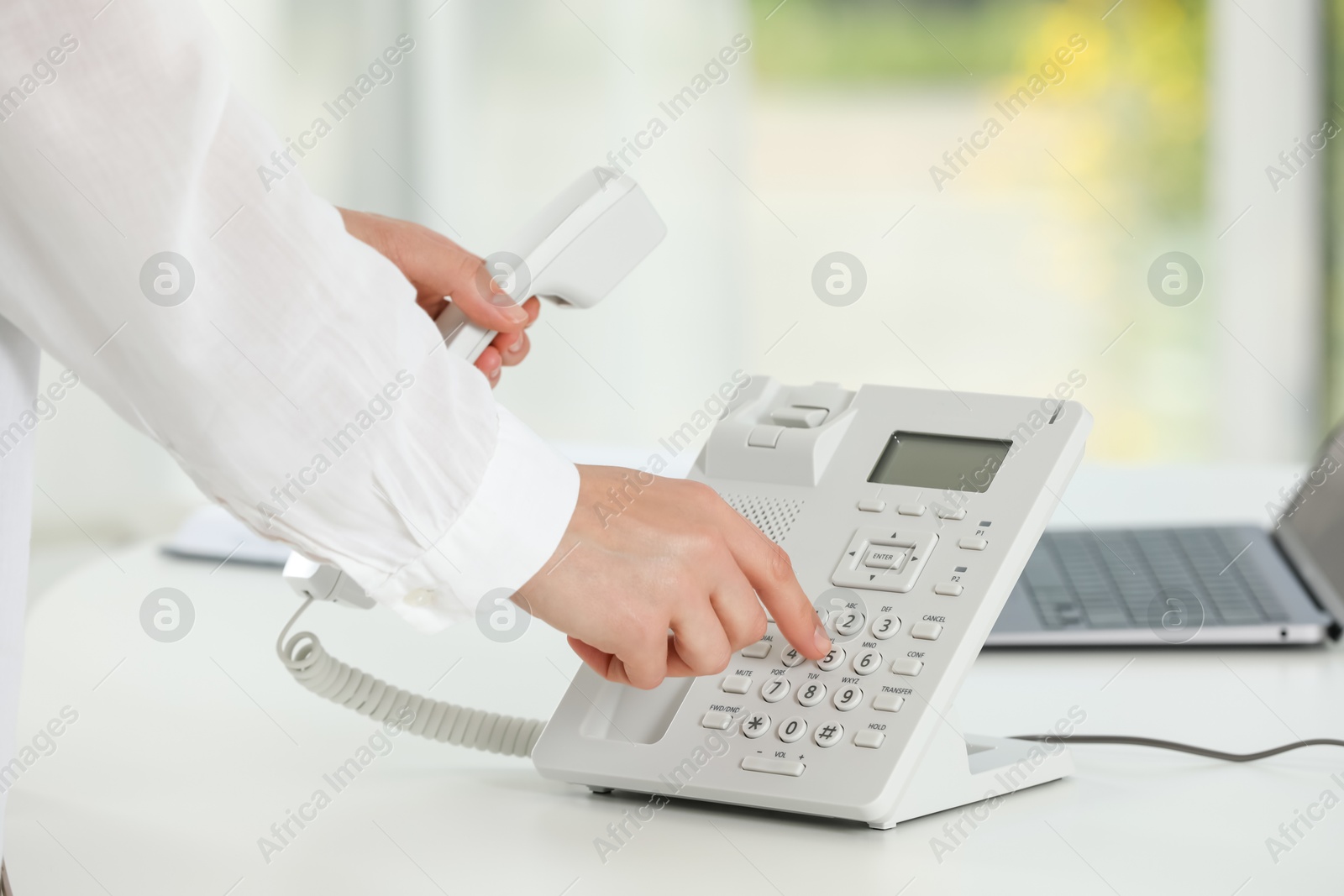 Photo of Assistant dialing number on telephone against blurred background, closeup