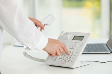 Photo of Assistant dialing number on telephone against blurred background, closeup