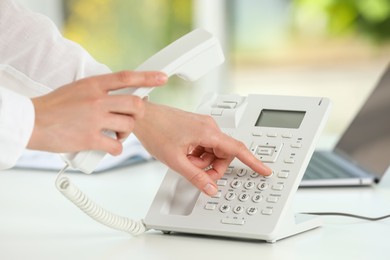 Photo of Assistant dialing number on telephone against blurred green background, closeup