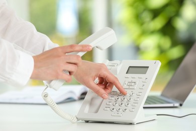 Photo of Assistant dialing number on telephone against blurred green background, closeup