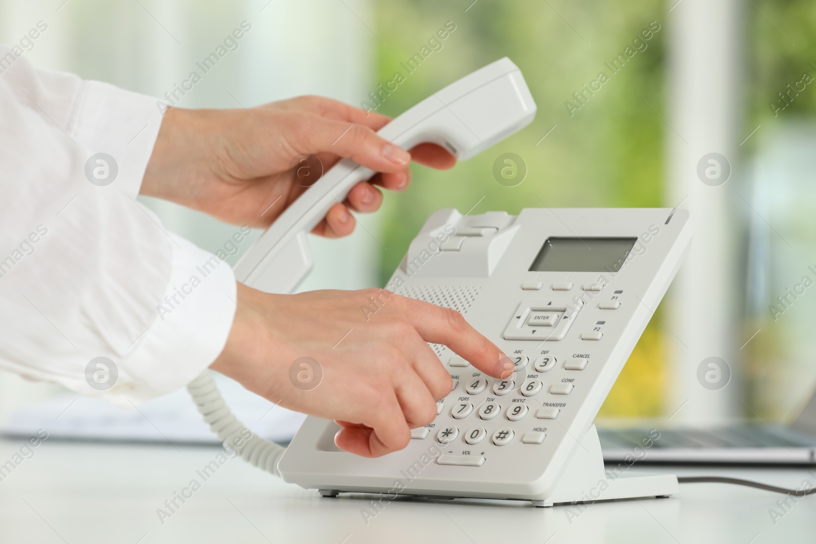 Photo of Assistant dialing number on telephone against blurred green background, closeup