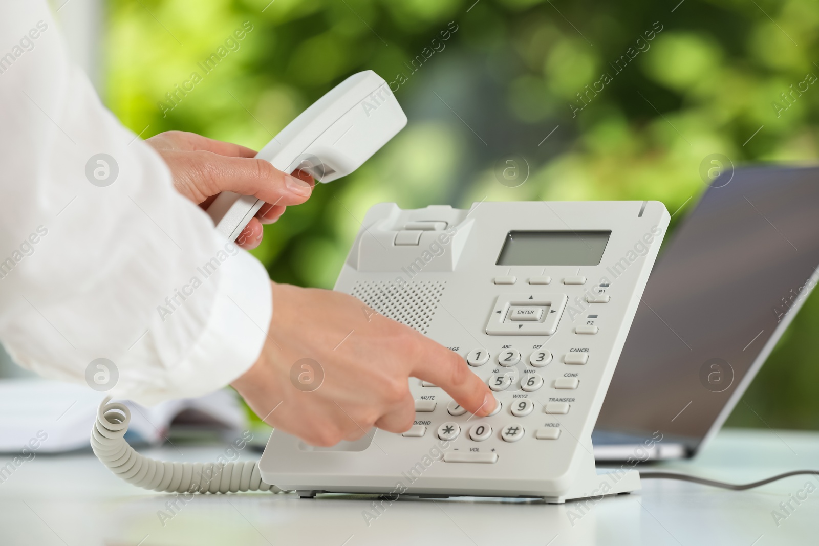 Photo of Assistant dialing number on telephone at table against blurred green background, closeup